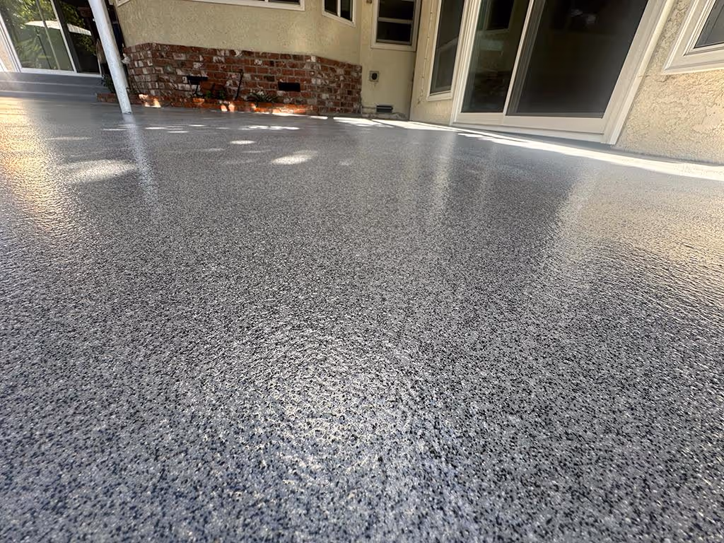 Close-up of a smooth, shiny gray quartz flooring on a patio area with light reflections and a brick accent wall in the background.
