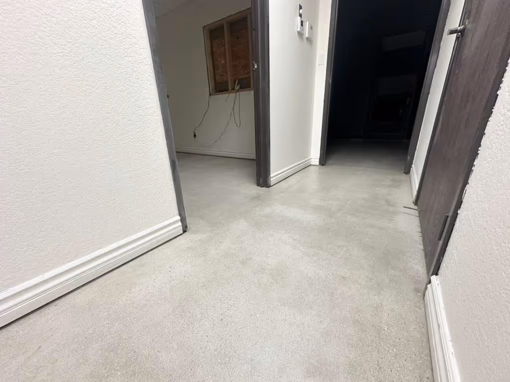 Smooth, light gray concrete floor in a hallway with white walls and dark door frames.