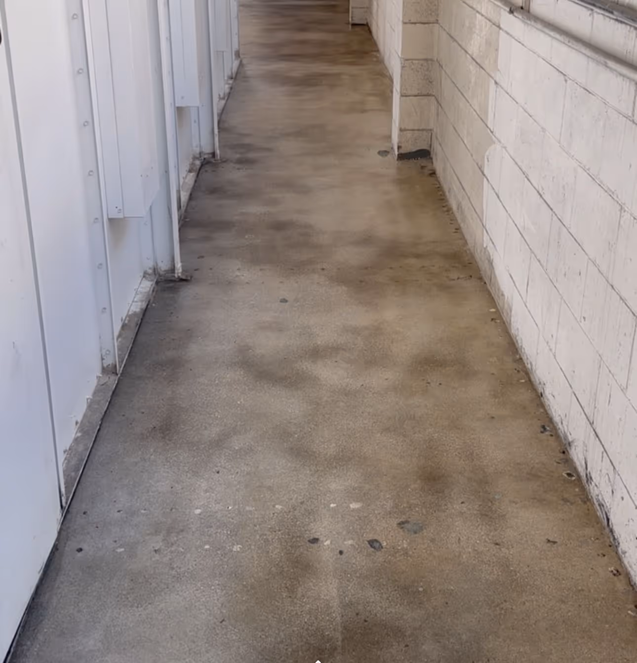 Narrow corridor with stained concrete floor and white walls on both sides.