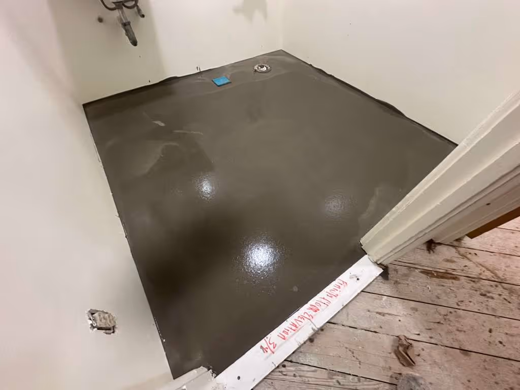Room corner with freshly poured and smoothed gray concrete self-leveling floor next to a wooden subfloor.