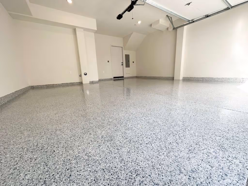Clean empty garage with light gray epoxy flake flooring and beige walls.