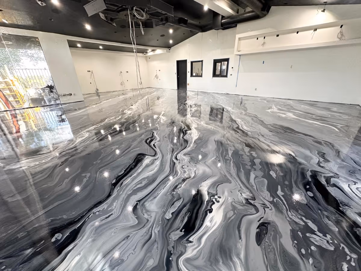Empty room with a glossy, marbled black and white epoxy floor and white walls under ceiling lights.