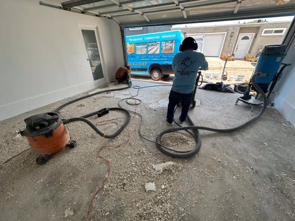 Two workers grinding a concrete garage floor with vacuum and grinding equipment during a floor resurfacing project.
