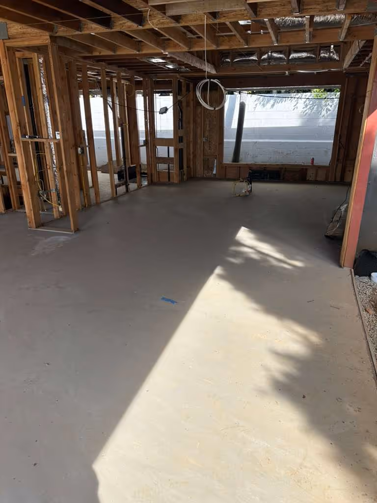 Interior view of a room under construction with wooden framing and a smooth, newly poured concrete floor.
