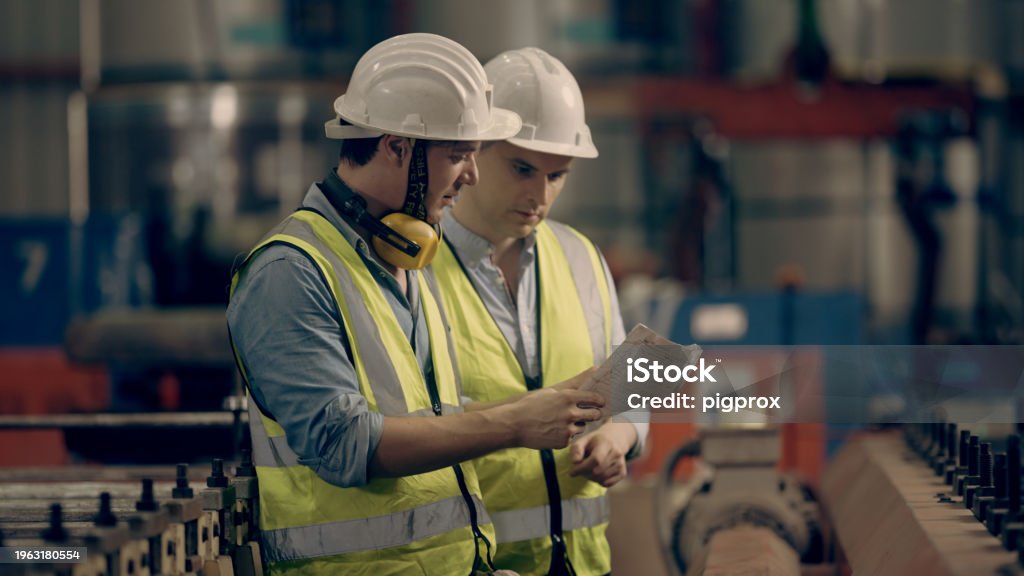 Workers holding helmets discuss GMG EnviroSafe safety compliance training in a warehouse setting