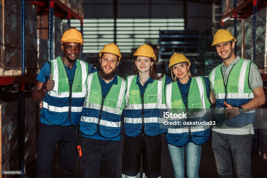 Workers holding helmets discuss GMG EnviroSafe safety compliance training in a warehouse setting
