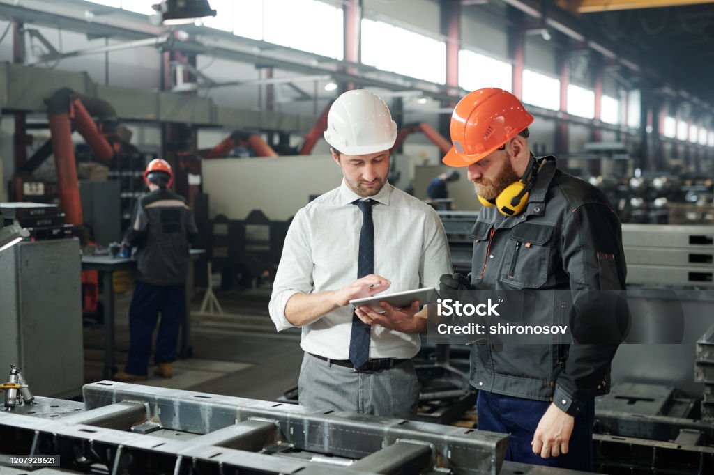 Workers holding helmets discuss GMG EnviroSafe safety compliance training in a warehouse setting