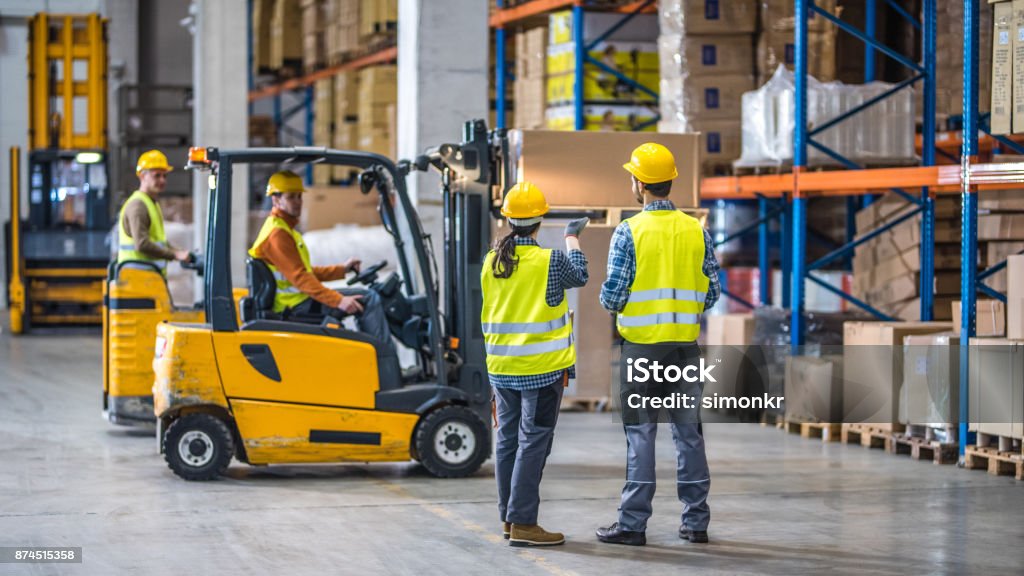 Workers holding helmets discuss GMG EnviroSafe safety compliance training in a warehouse setting