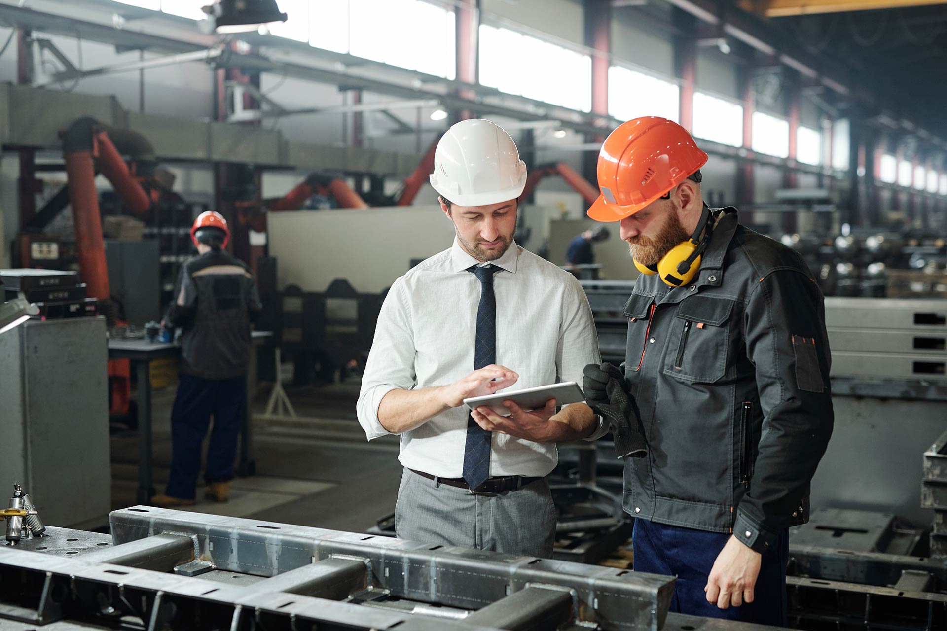 Workers holding helmets discuss GMG EnviroSafe safety compliance training in a warehouse setting