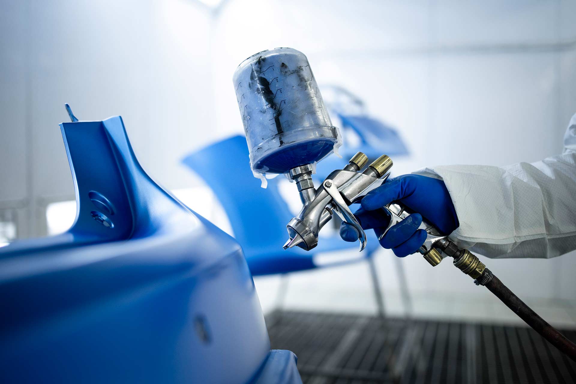 Technician spray painting car with GMG's EHS-compliant collision repair solutions