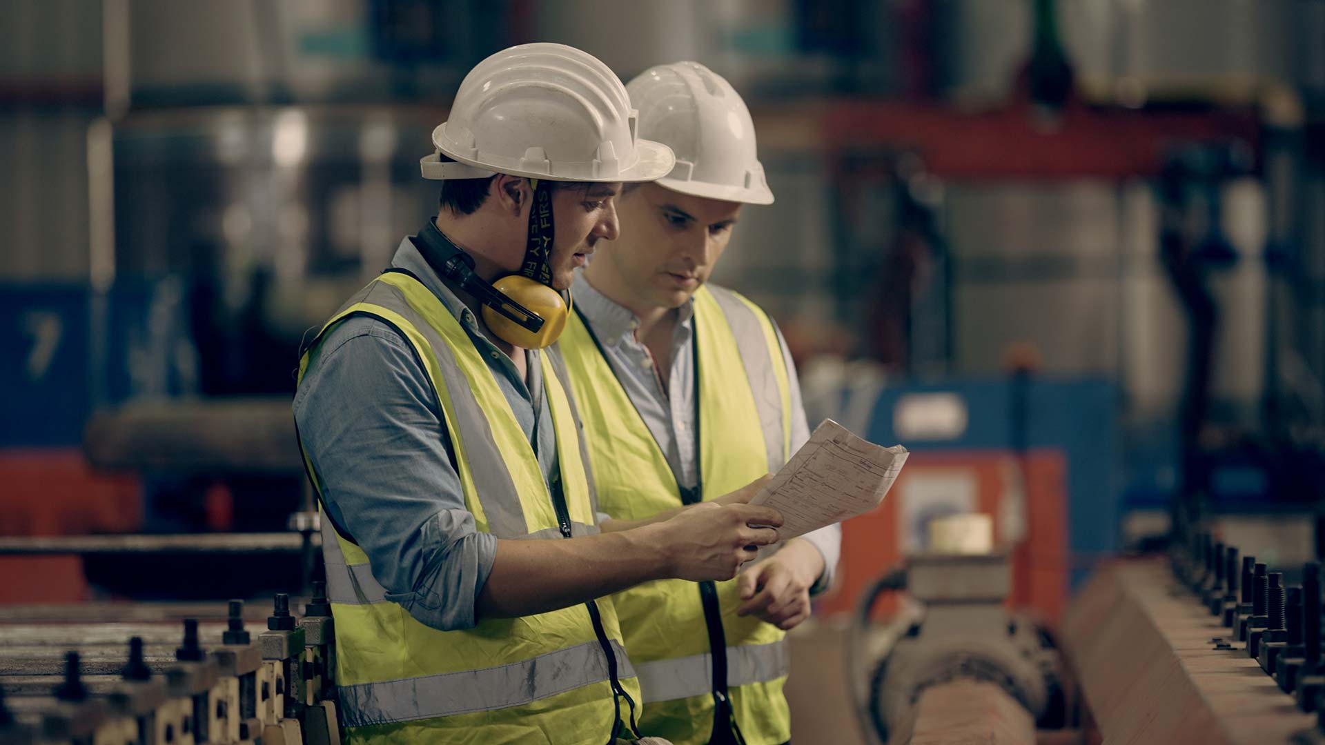 Workers holding helmets discuss GMG EnviroSafe safety compliance training in a warehouse setting