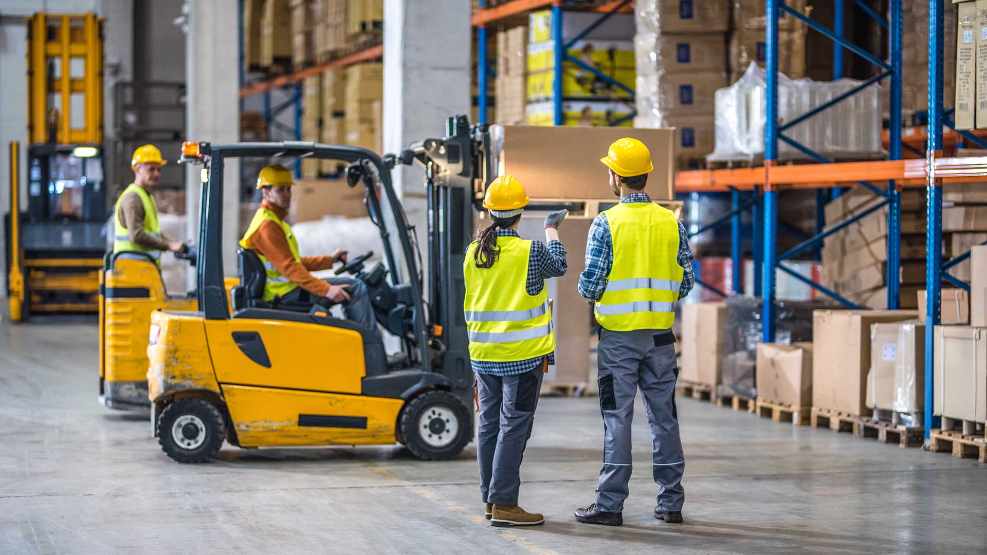 Workers holding helmets discuss GMG EnviroSafe safety compliance training in a warehouse setting