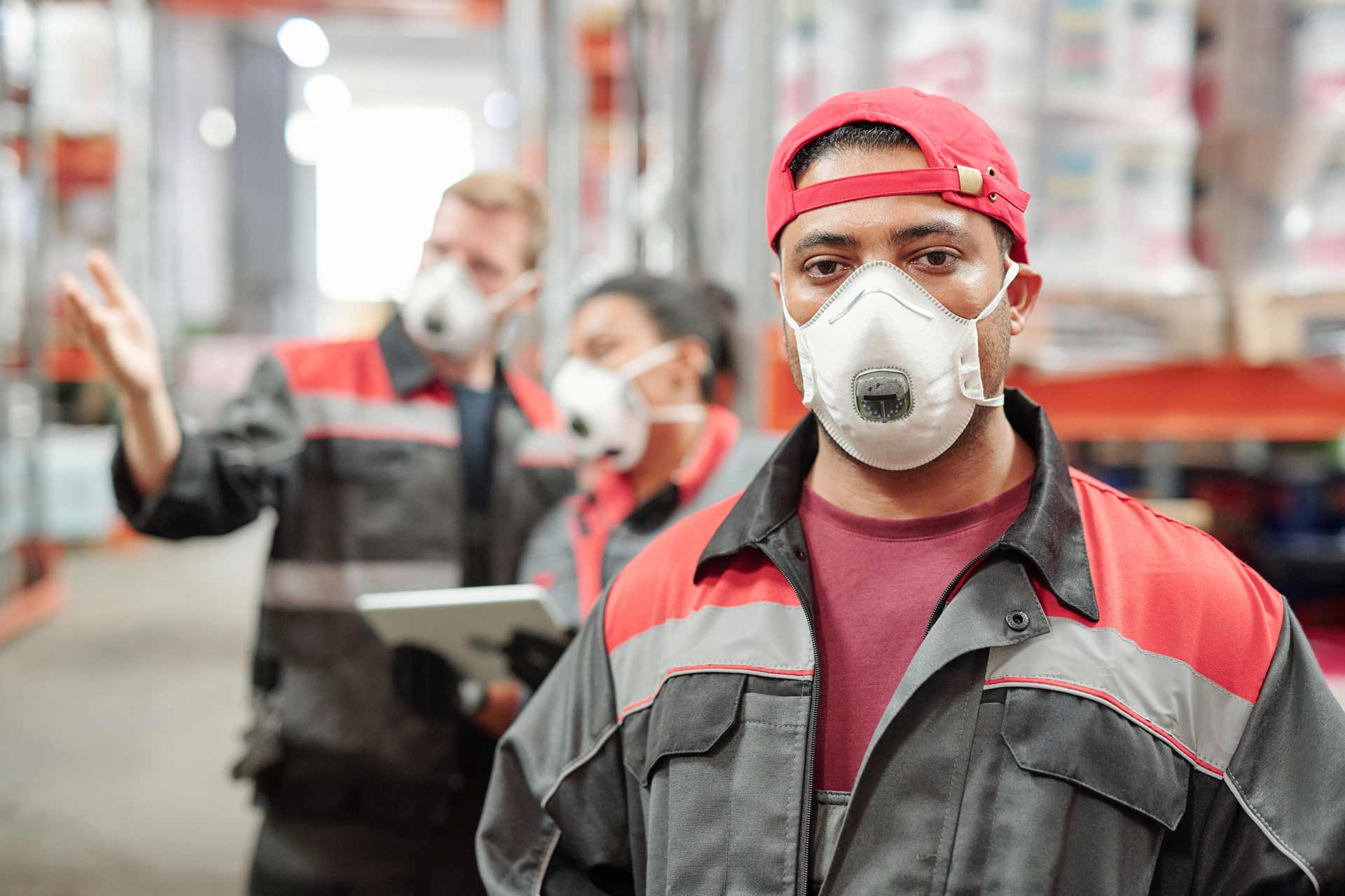 Workers holding helmets discuss GMG EnviroSafe safety compliance training in a warehouse setting