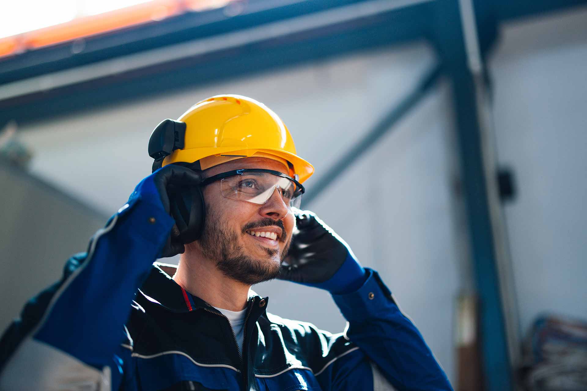 Workers holding helmets discuss GMG EnviroSafe safety compliance training in a warehouse setting
