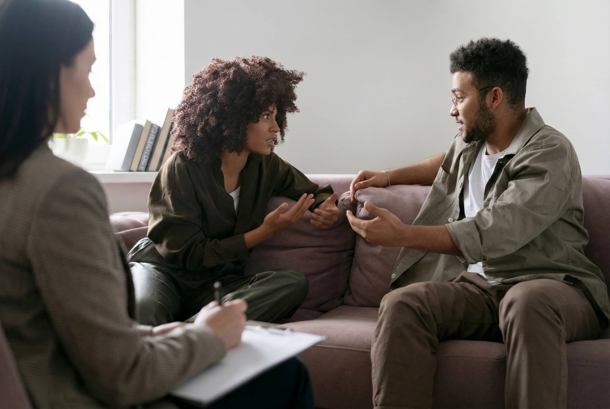 A diverse couple engages in couples therapy, speaking with each other while a female therapist observes and supports healthy communication.