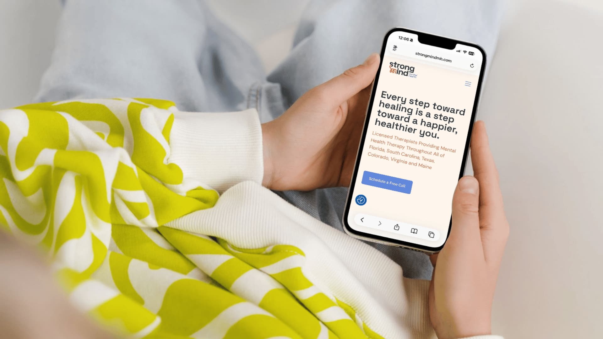 A person holds a smartphone while preparing to fill out an online therapy consultation form on the Strong Mind Mental Health website.