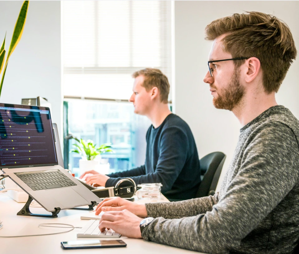 two men sitting at a desk working on a laptop