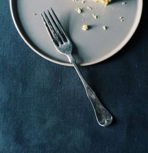 Plate with crumbs and a silver fork on black linen tablecloth by professional photographer Mark Weinberg