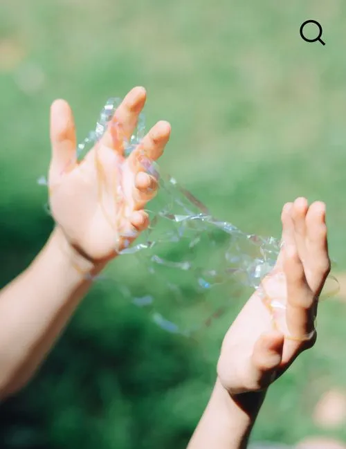 VSCO Search icon overlaid on a picture of two hands holding tangled clear ribbon with a blurred green background