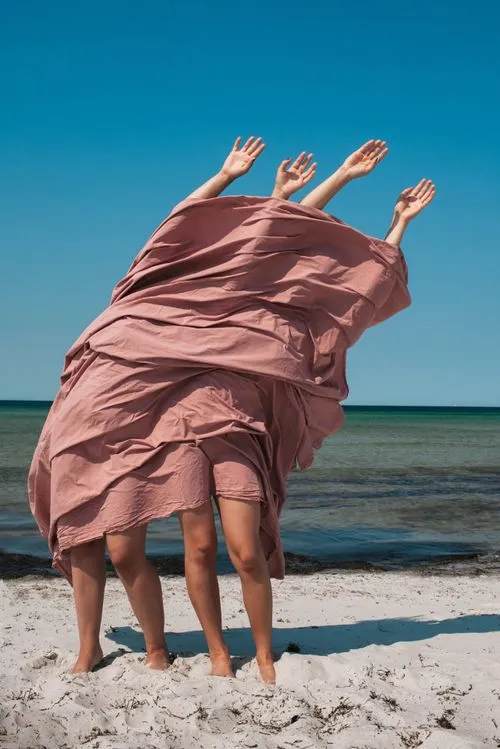 Two people on a beach with their hands raised in the air with pink cloth covering their bodies by Tanya Borodina
