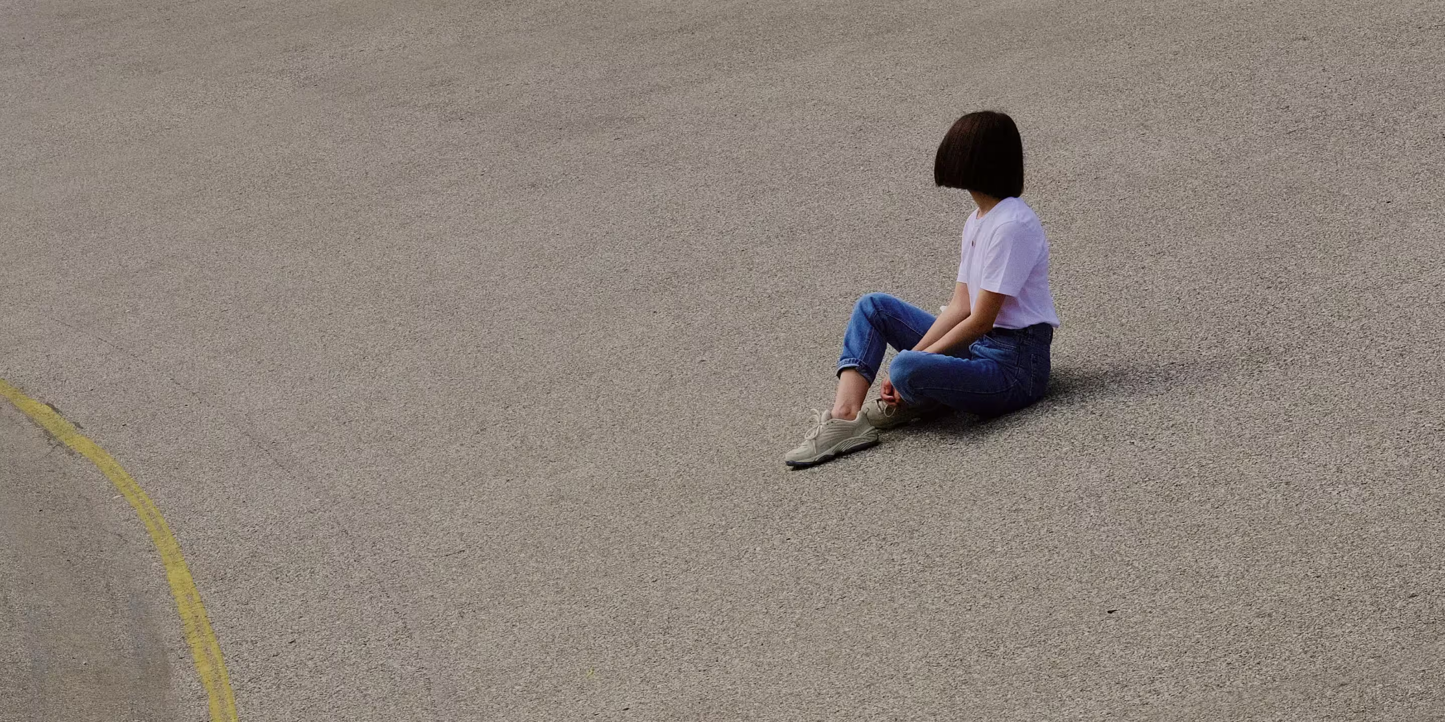 Woman in t shirt and jeans sitting on slanted cement looking away