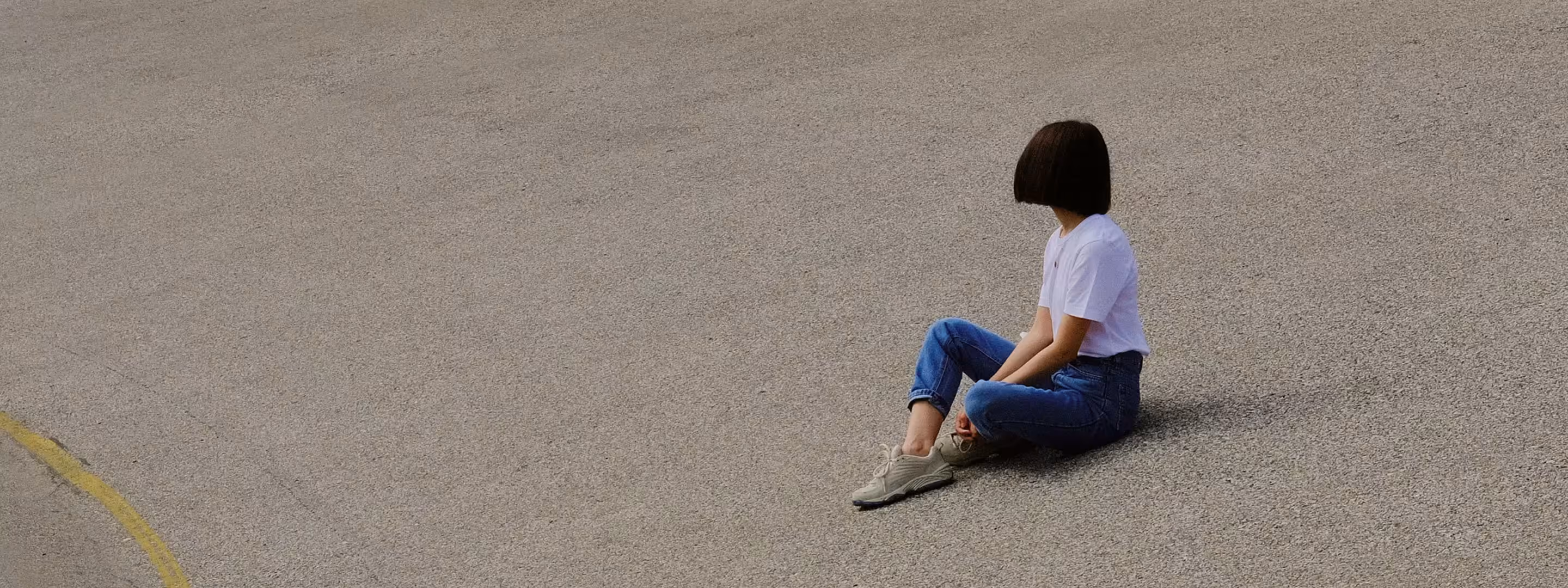 Mulher de camiseta e jeans sentada no cimento inclinado olhando para longe