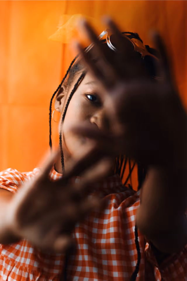 Selective brightening of photo of girl holding hands in front of her face with orange background