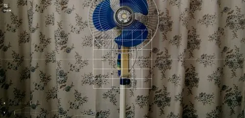 VSCO skew image tool overlaying x and y axis to edit photo of a blue fan in front of beige curtains with floral pattern