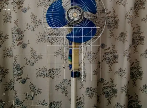 VSCO skew image tool overlaying x and y axis to edit photo of a blue fan in front of beige curtains with floral pattern