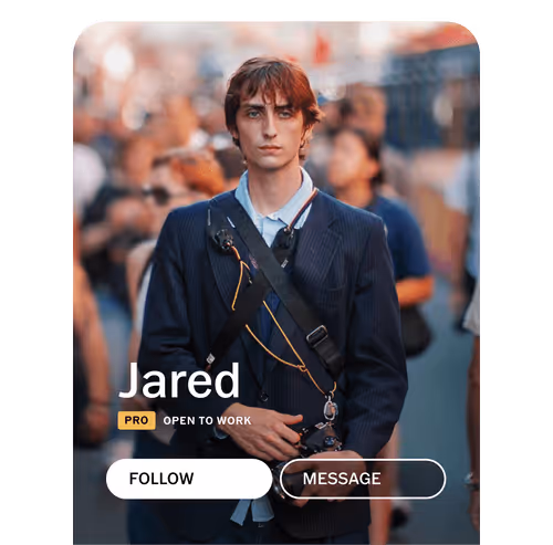 VSCO community profile for photographer Jared wearing a navy blazer holding a camera with a strap across his chest, standing on a busy street with profile UI labels PRO, Open for Work, Follow, and Message
