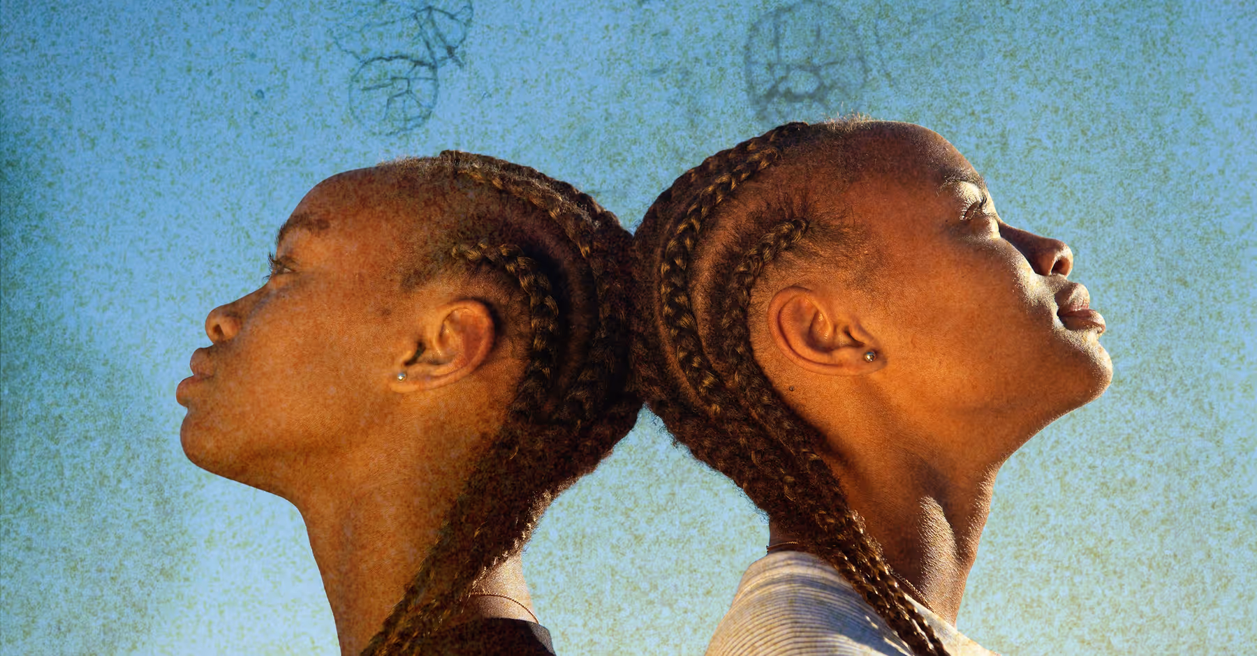 Two people with braided hair standing back to back against a blue sky with an expired film textured overlay for a vintage distressed effect.