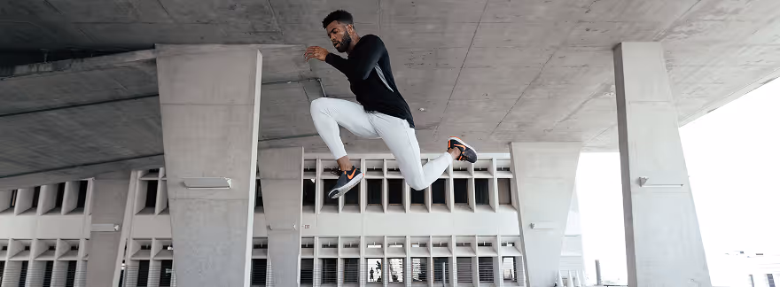 Athletic man in black shirt and white pants jumping mid-air under a concrete structure.