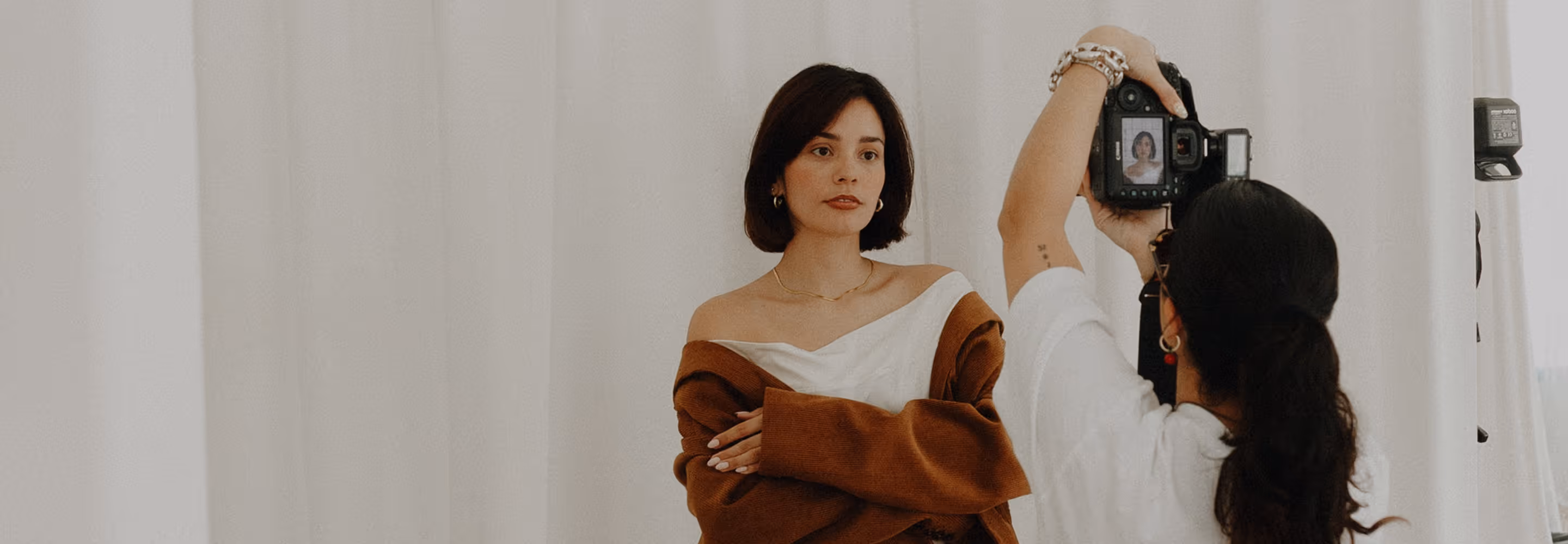 Woman in brown cardigan and white top posing for a photo being taken by a photographer with a professional camera against a white backdrop.