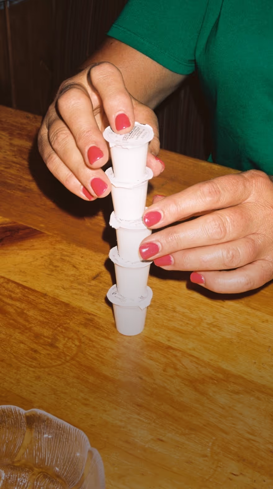 Hands with red nail polish stacking five small white creamer cups on a wooden table, taken by commercial photographer Cody Guilfoyle.
