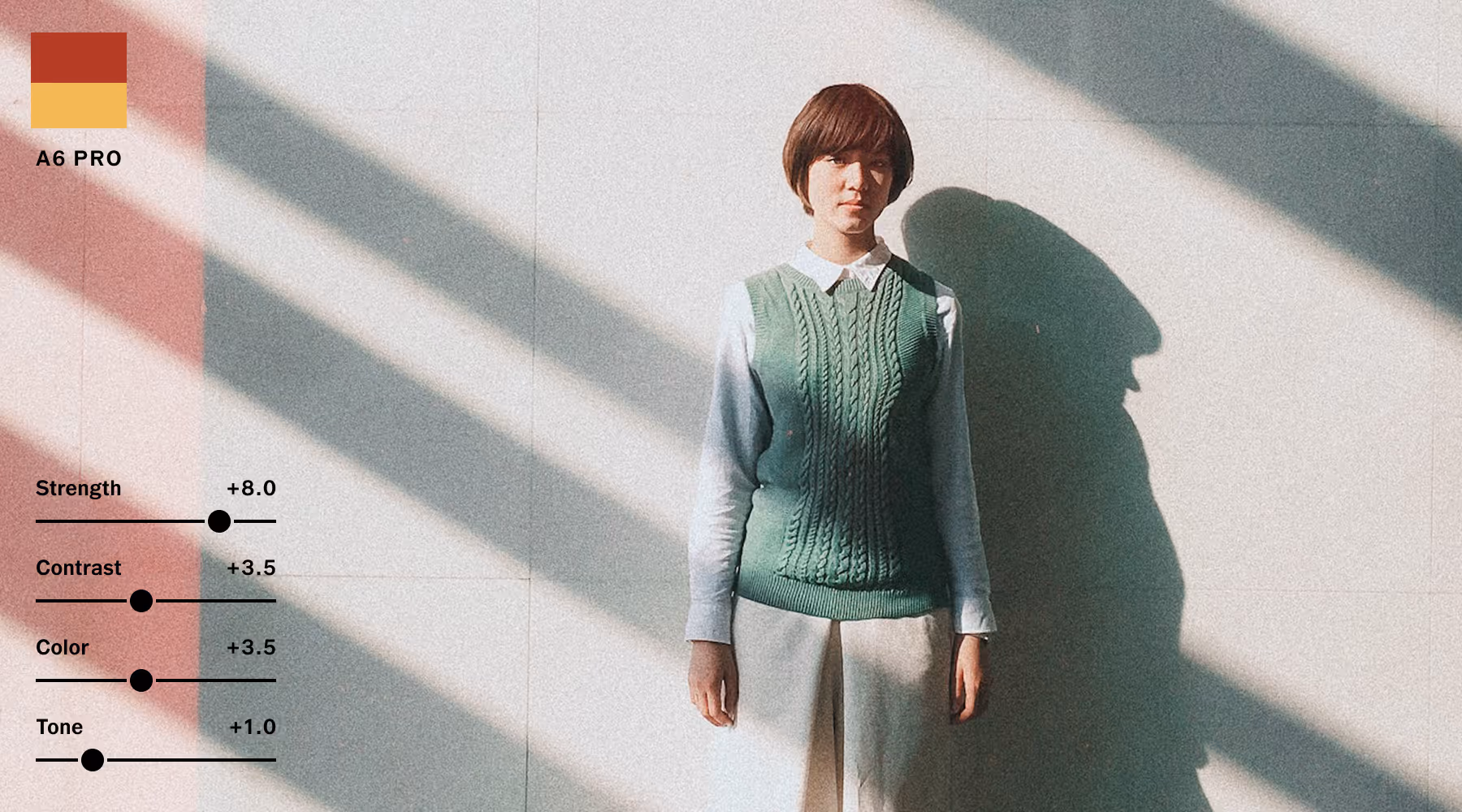 A6 PRO preset applied to image of person with short hair wearing a green knitted vest and white shirt standing against a wall with diagonal shadows.