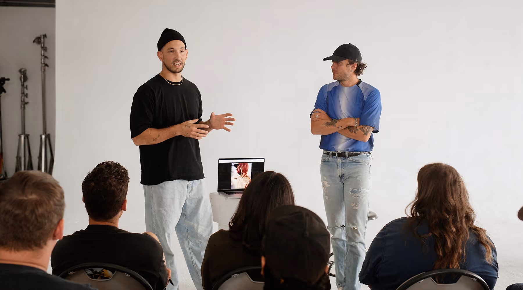 Two photographers standing and talking in front of a seated audience at a group session with TFP