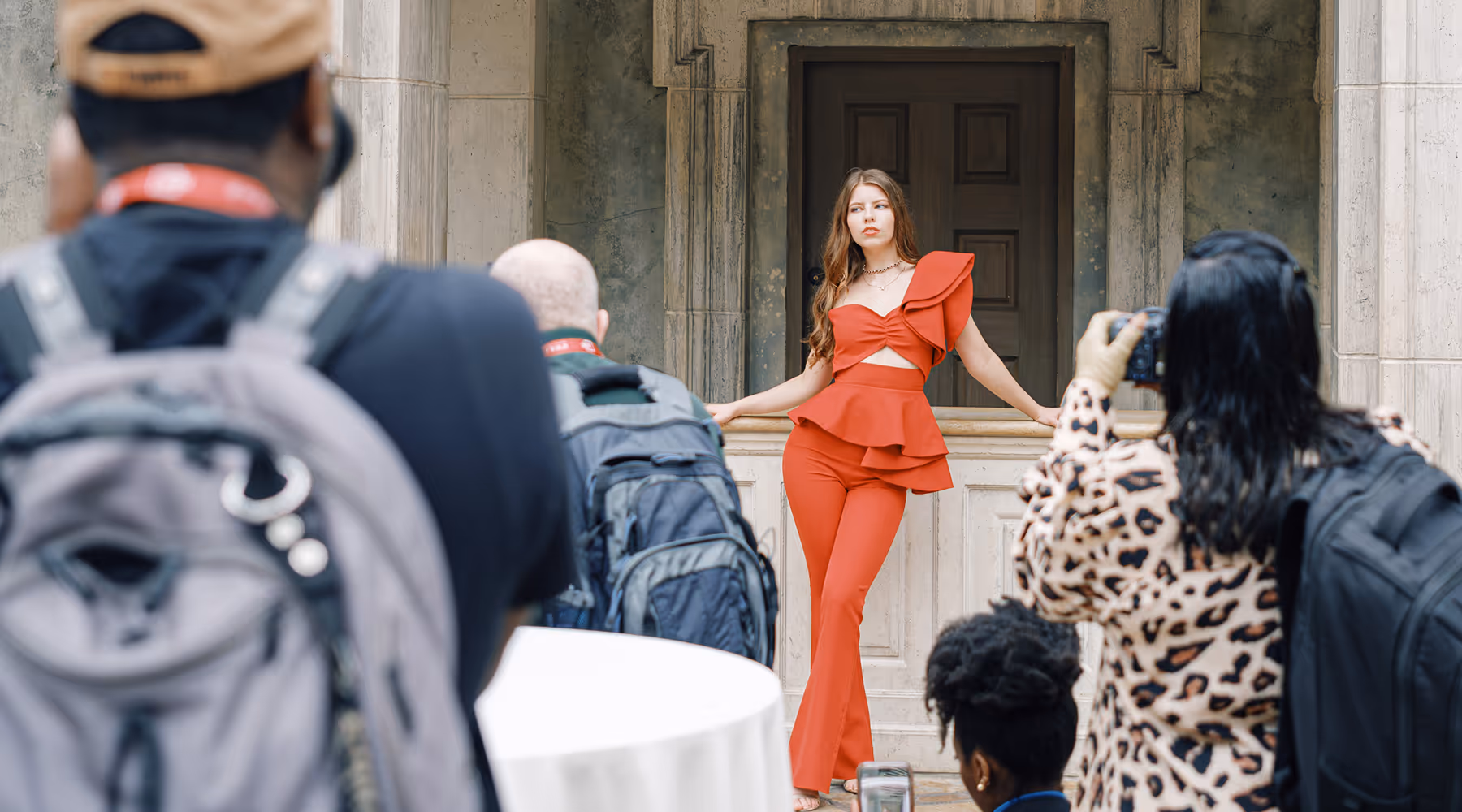 Practice photoshoot on a photo walk with a woman in a red outfit posing against a stone balcony with photographers taking pictures.