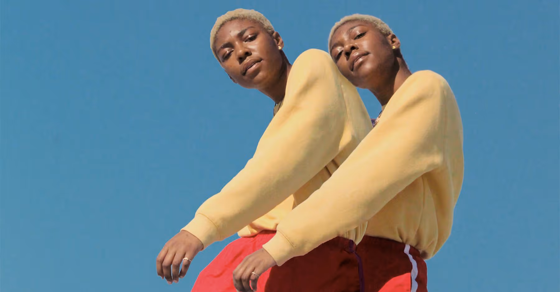 Saturated collage photo of person with short blonde hair wearing yellow sweaters and red pants against a clear blue sky.