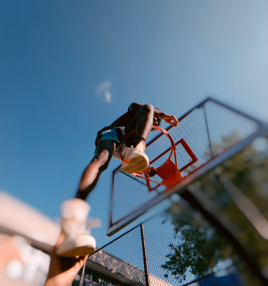 Photo blur effect applied to low-angle view of a basketball player mid-air about to dunk on an outdoor court under clear blue sky.