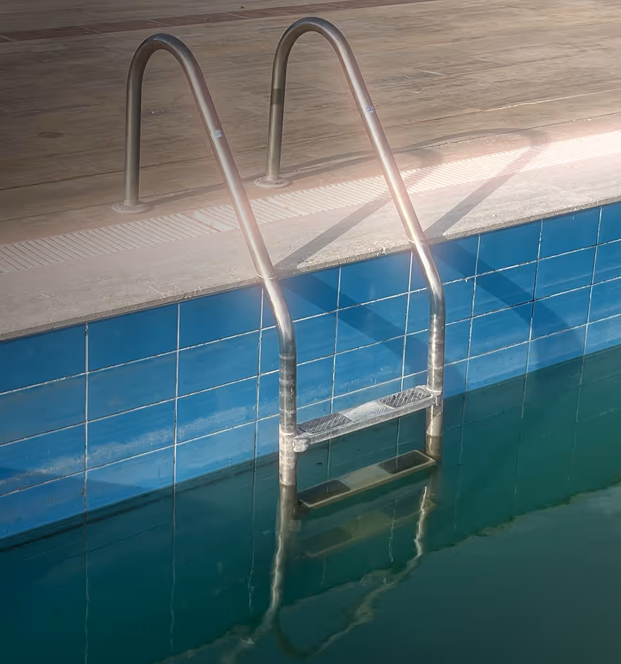 Halation added to metal ladder descending into a swimming pool with blue tiled walls and calm water reflecting the ladder.