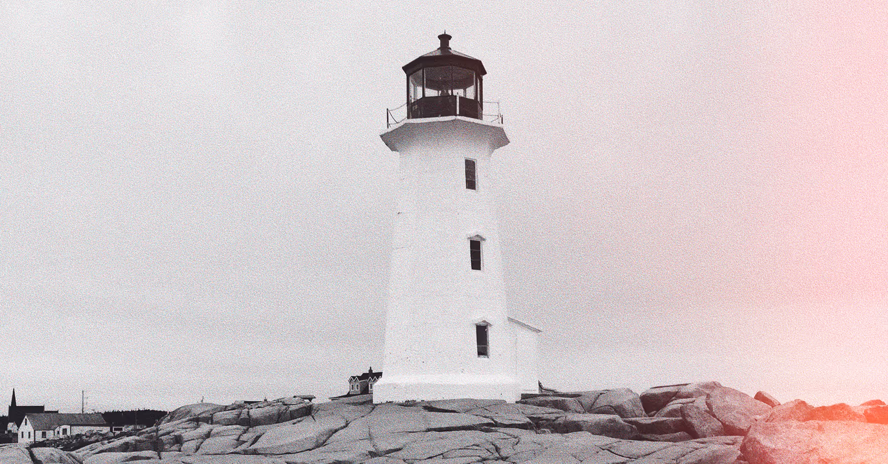 Cinematic photo of a white lighthouse on rocky shore with a few buildings and cloudy sky in the background, in black and white with a pink light leak effect.