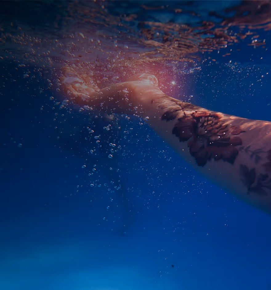 Halation effect on an underwater view of an arm with a floral tattoo reaching towards the water surface surrounded by bubbles.