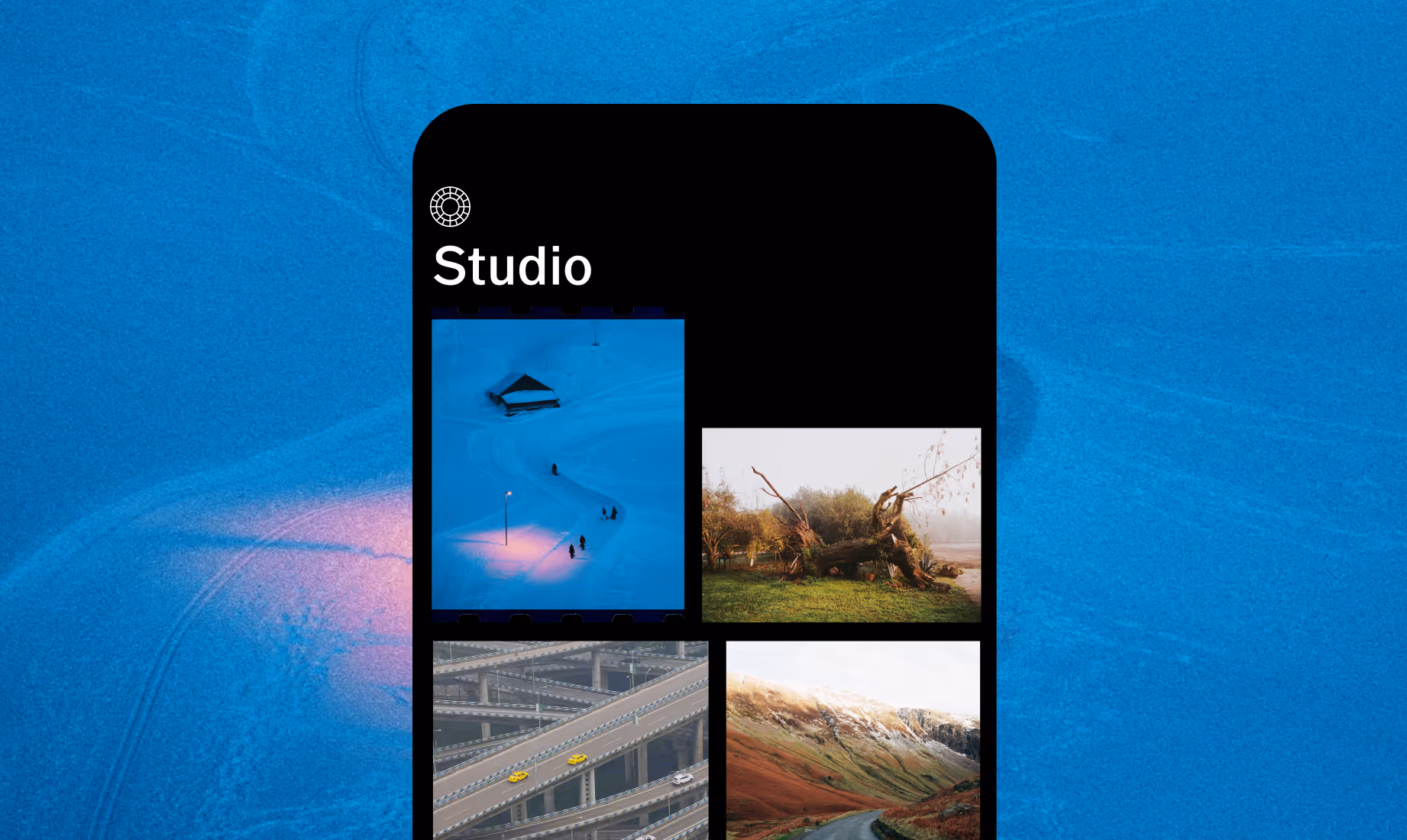 Smartphone screen showing a grid of photos in the VSCO Studio with images of snowy landscape with streetlamp and people, fallen tree in a field, highway interchanges with cars, and a mountain road.