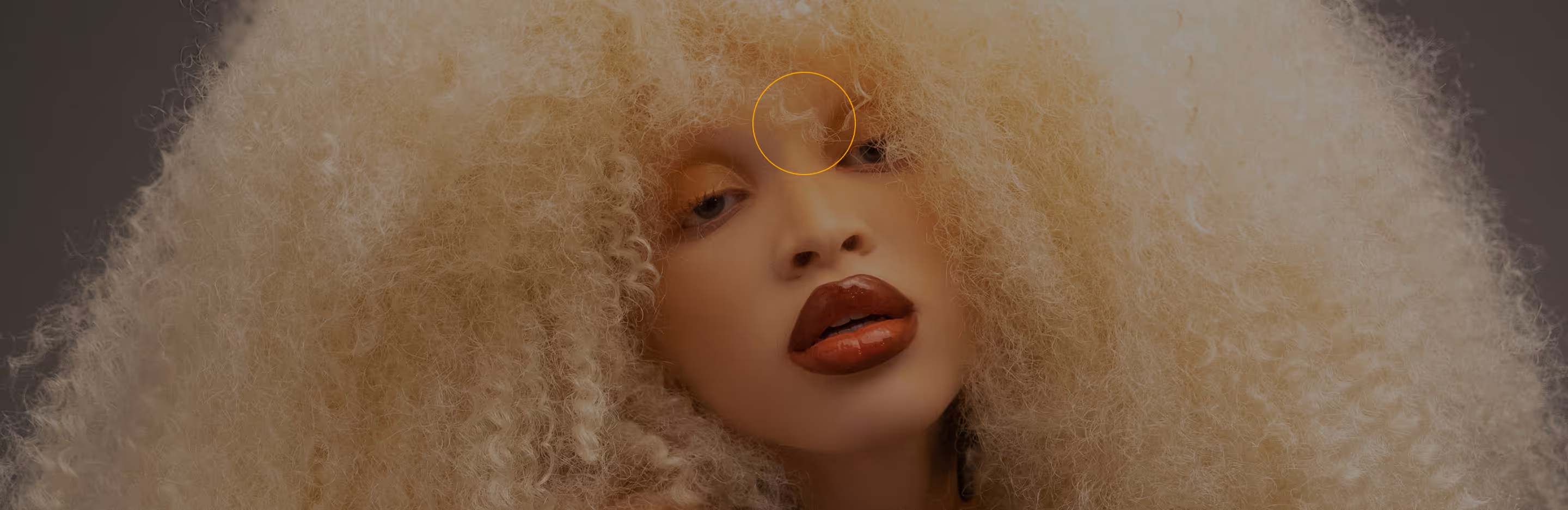 Close-up of a person with voluminous curly blonde hair and glossy red lips with a removal brush over a flyaway hair that will be removed with the AI editor.