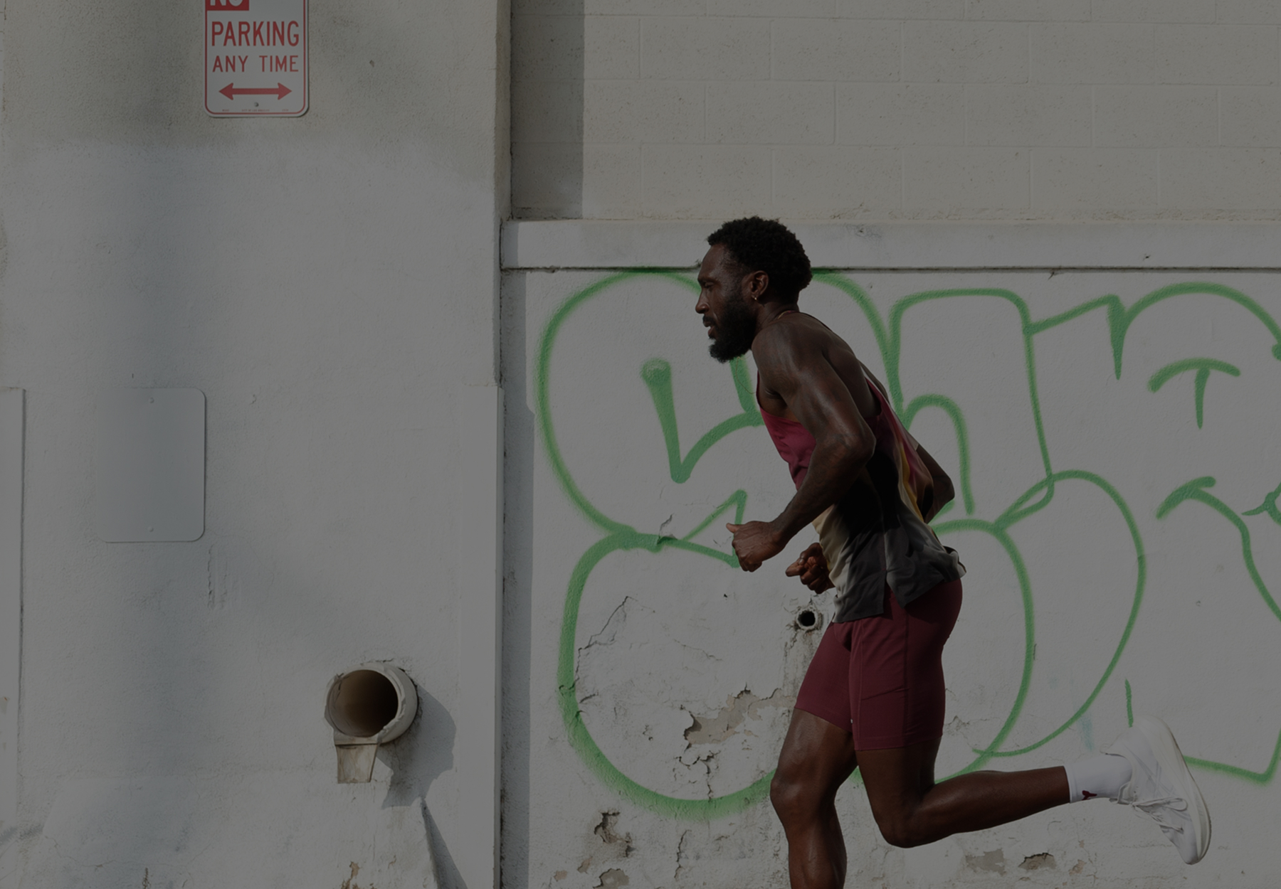 Man running outdoors next to a wall with green graffiti and a no parking sign, before being cleaned up with AI removal tool.