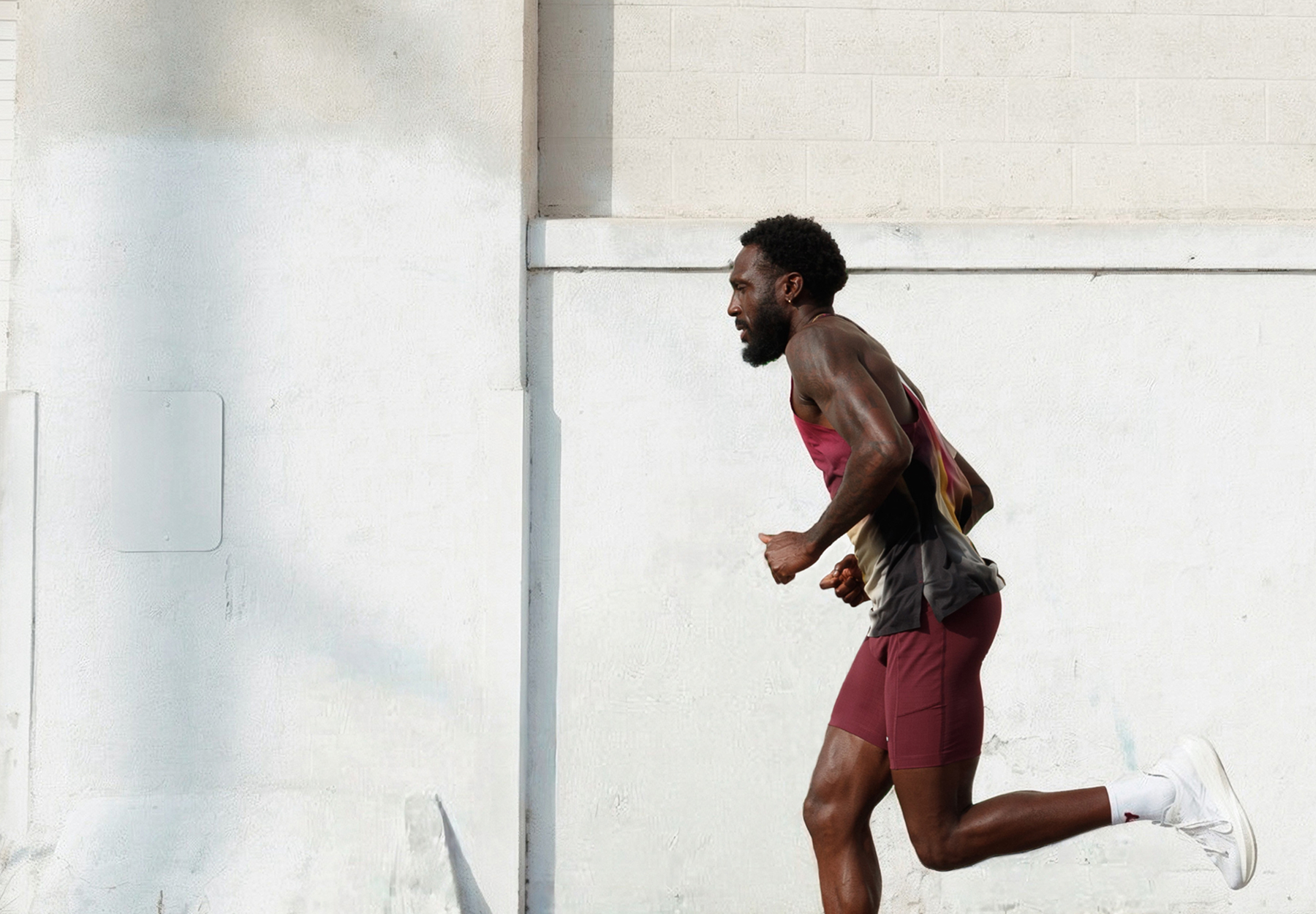Professional photoshoot of a man running outdoors against a white wall that was cleaned up with AI background removal tool.