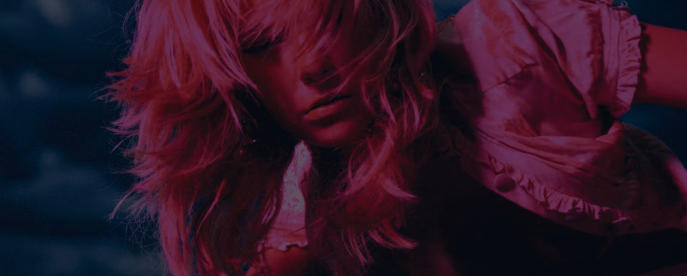 Close-up of a person with long hair partially covering their face, lit with pinkish-purple lighting.