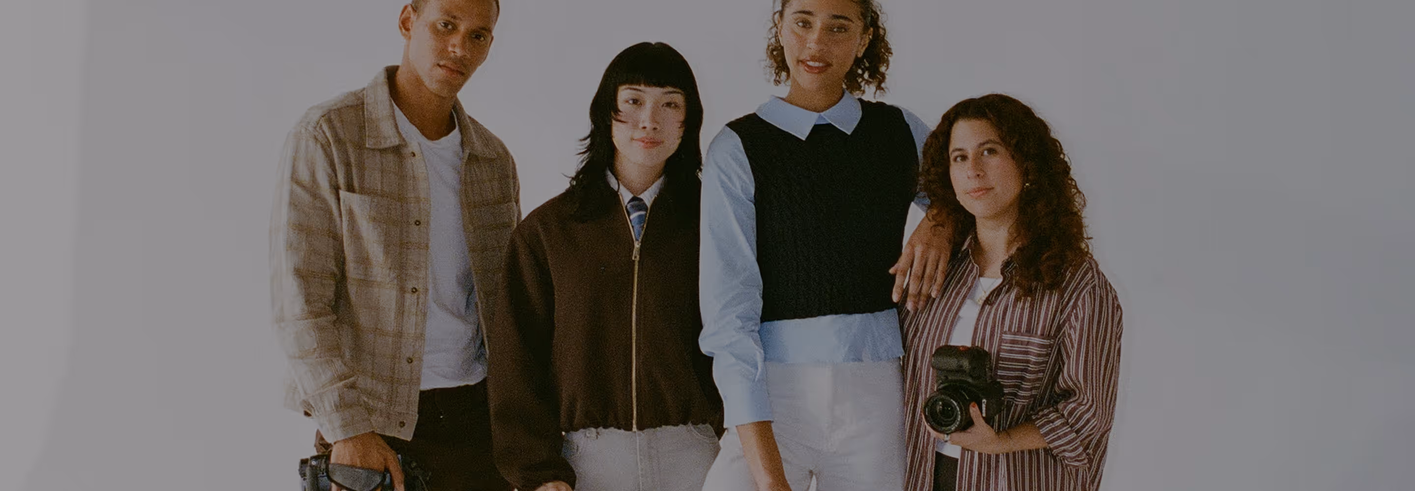 Group of four diverse photographers standing together and holding cameras with a white backdrop.