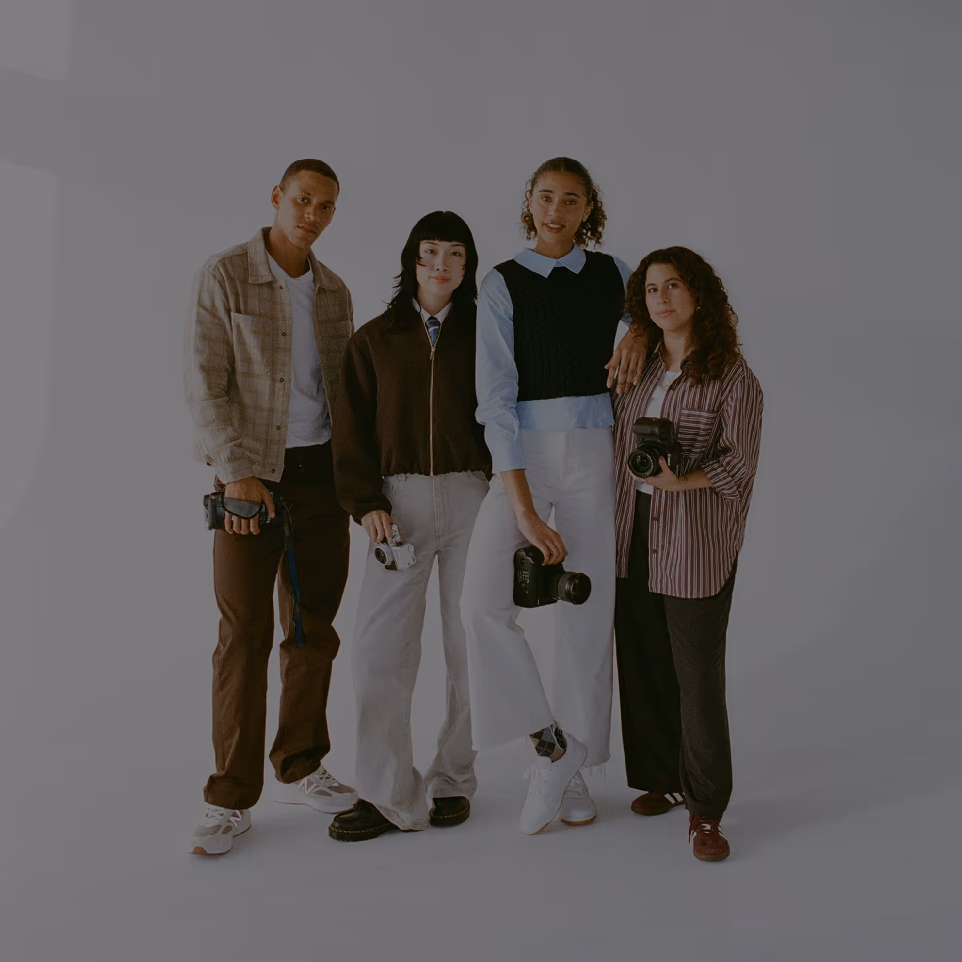 Group of four diverse photographers standing together and holding cameras with a white backdrop.