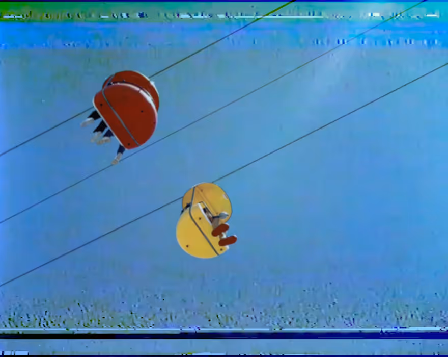 VHS filter on two colorful gondola cable cars suspended on wires against a clear blue sky.